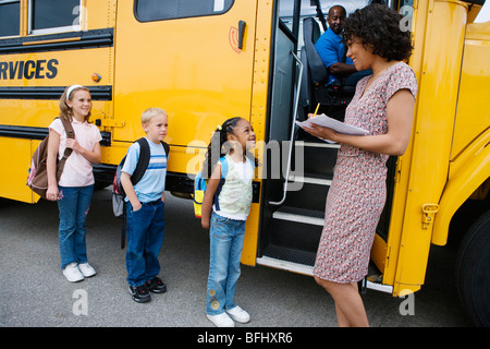 Lehrer laden Grundschüler auf Schulbus Stockfoto