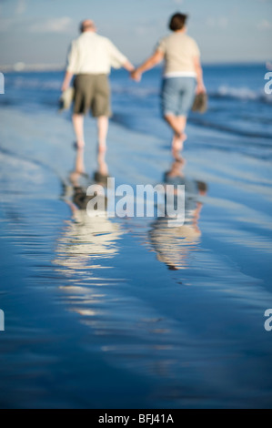 Älteres Paar zu Fuß am Strand, im Wasser reflektiert Stockfoto