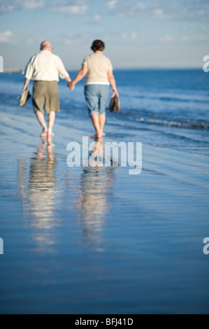 Älteres Paar zu Fuß am Strand, im Wasser reflektiert Stockfoto