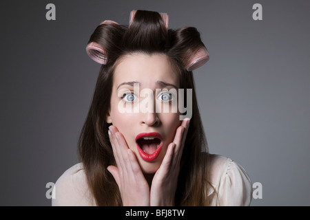Überrascht, junge Frau mit Lockenwickler und roten Lippenstift Stockfoto