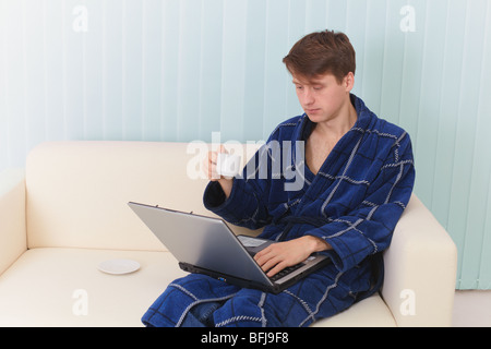 Der Mann arbeitet auf dem Haus Internet auf einem Sofa und trinkt Kaffee Stockfoto