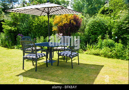 Gartenmöbel und Sonnenschirm auf einer Wiese in einem typisch englischen Stadt oder Land festgelegten Garten im Sommer Stockfoto