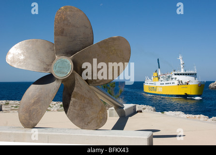 Eine gelbe Fähre betreten Ciutedella Hafen gegen ein Schiff Propeller Denkmal gesetzt Stockfoto