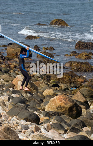 Teen mit Surfbrett, das Wasser am Point Judith Lighthouse in Rhode Island zu erreichen. Stockfoto