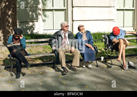 alte jüdische Paare genießen Sie die Sonne auf einer Bank in New York City Hall Park neben junge schwarze Frau & dösen barfuß junger Mann Stockfoto