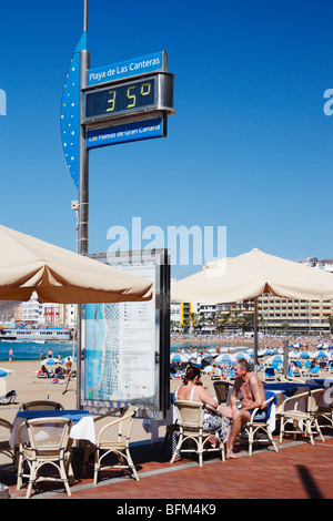 Paar auf Terrasse mit Blick auf Playa de Las Canteras in Las Palmas auf Gran Canaria. Temperatur-Messgerät zeigt 35 Grad. Stockfoto