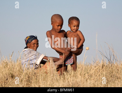 Botswana, Makgadikgadi. Buschmänner Kinder spielen in die trockene Gräser der Kalahari, beobachtet von ihrer Mutter. Stockfoto