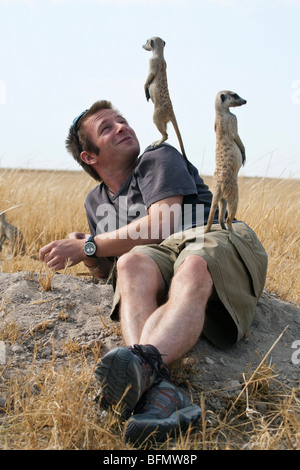 Botswana, Makgadikgadi. Ein junger Mann verlegen zurück mit Erdmännchen mit ihm als einem Aussichtspunkt. Stockfoto