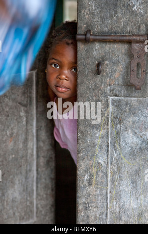 Tansania, Sansibar. Ein junges Mädchen guckt heraus von der Haustür ihres Hauses in Nungwi, der Nordspitze der Insel Sansibar. Stockfoto