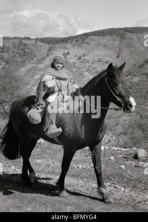 Chile, Patagonien.  Ein Junge trägt ein Lamm über seinem Sattel während Viehtreiber Schafe. Stockfoto