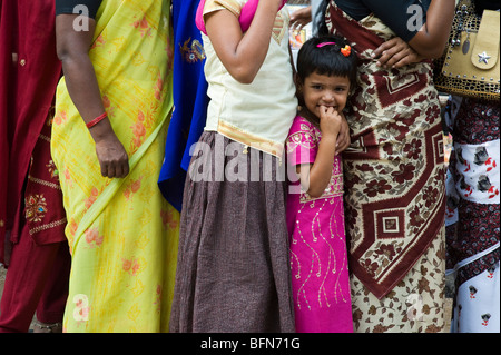 Kleine indische Mädchen stehen in zwischen Damen tragen bunte Sari's in einer Warteschlange in Puttaparthi, Andhra Pradesh, Indien Stockfoto