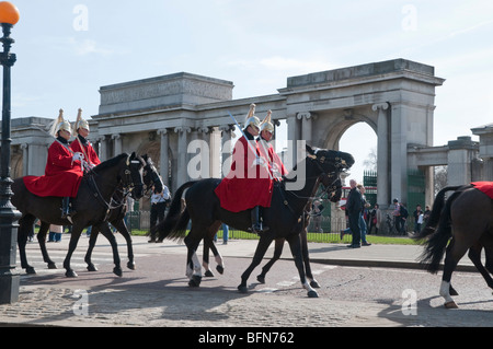 Wachen in rote Tuniken und gefiederte Helme fahren vor Bögen am Hyde Park corner Stockfoto