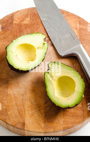 Avocado in Scheiben geschnitten in der Hälfte auf Bambus Schneidebrett mit Messer Stockfoto