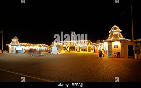 Touristen gehen in einer Unschärfe hinter dem Eingang zum Brighton Pier in der Nacht Stockfoto