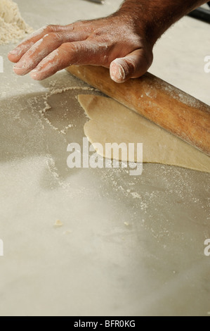 Ein Koch Teig auf der Arbeitsfläche mit einem Nudelholz ausrollen. Stockfoto
