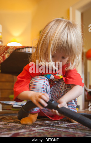 Junge mit langen blonden Haaren hilft mit Staubsaugen Stockfoto