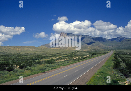 Eine lange, schmale Straße führt in Guadalupe Mountains Nationalpark unter einem blauen Himmel voller Wolken, in West-Texas Stockfoto
