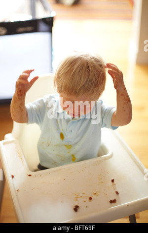 Baby Boy in einen Hochstuhl, ein Chaos mit seinem Essen Stockfoto