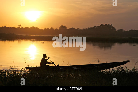 Fischer in ein kleines Boot überqueren einen Fluss bei Sonnenuntergang Stockfoto