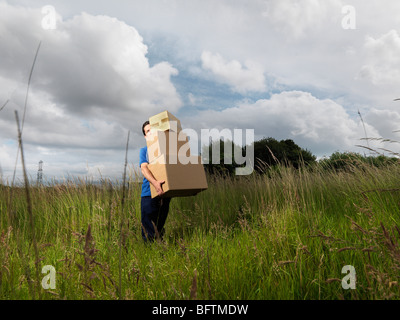 Mann trägt Boxen durch Feld Stockfoto