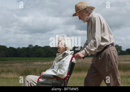 Älterer Mann, die Frau im Rollstuhl schieben Stockfoto