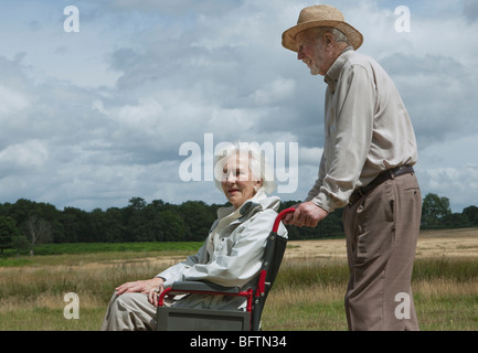 Älterer Mann, die Frau im Rollstuhl schieben Stockfoto