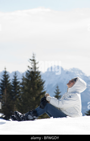 Junge Frau sitzt im Schnee im Winter-Szene Stockfoto