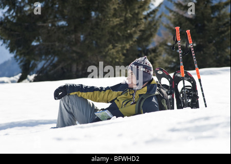 Junger Mann sitzen im Schnee mit Wanderausrüstung Stockfoto