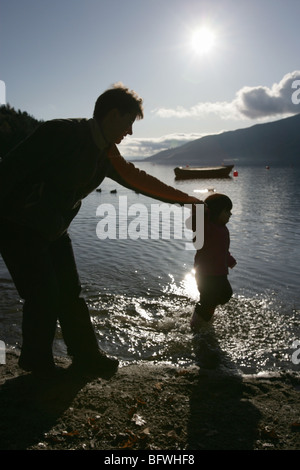 Bereich der Loch Lomond, Schottland. Silhouette Blick auf eine Mutter und Tochter Händchen, während im Wasser paddeln. Stockfoto