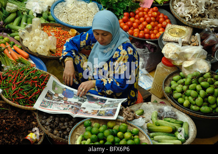 Malaysische oder malaysische muslimische Frau in Head Scarf Reading Malaysische Zeitung, Central Fruit & Vegetable Market, Kota Bahru, Malaysia Stockfoto