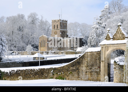 Oxfordshire Kirche in Sonnenschein und frisch gefallenem Schnee mit einem sanften blauen Himmel dahinter. Tor vor.  Schneebedeckte Bäume. Stockfoto