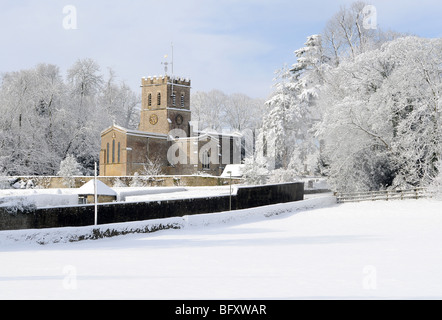 Oxfordshire Kirche in Sonnenschein und frisch gefallenem Schnee mit einem sanften blauen Himmel dahinter.  Felder im Vordergrund.  Schneebedeckte Bäume. Stockfoto