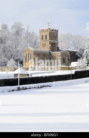 Oxfordshire Kirche in Sonnenschein und frisch gefallenem Schnee mit einem sanften blauen Himmel dahinter.  Felder im Vordergrund. Stockfoto