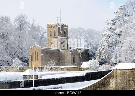 Oxfordshire Kirche in Sonnenschein und frisch gefallenem Schnee mit einem sanften blauen Himmel dahinter. Wände im Vordergrund.  Schneebedeckte Bäume. Stockfoto