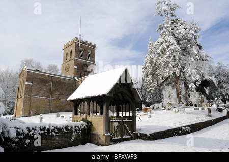 Eine Kirche in Oxfordshire von unten in die Sonne und Schnee mit den Lychgate im Vordergrund.  Blauer Himmel und Wolken hinter Stockfoto