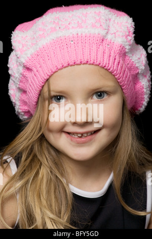 wunderschönes kleines Mädchen mit langen Haaren in rosa Hut auf schwarzem Hintergrund Stockfoto