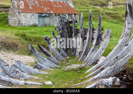 Das Skelett von einem zerstörten Fischerboot am Strand vor einer alten Fischerhütte am Talmine, Highland, Schottland Stockfoto