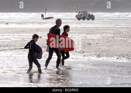 Vater und Söhne zu Fuß am Strand mit Surfbrettern Stockfoto