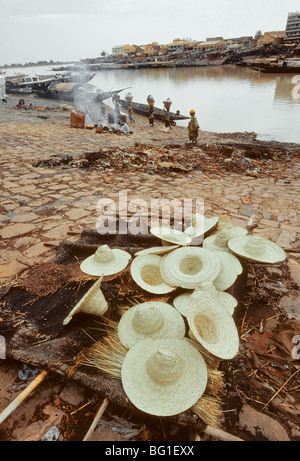 Strohhüte sind für den Verkauf am Ufer des Niger in Mopti, Mali, Westafrika, und eine Gruppe von Frauen, die Träger sind das Laden liefert auf eine große Piroge zum Transport in Timbukto Stockfoto