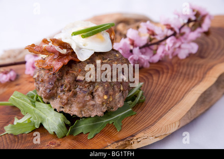 Gourmet Burger auf Rakete Bett, mit Speck und Wachtelei auf und serviert auf Holz- platte mit wilden Blumen. Stockfoto