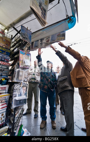 Lesen Sie die Schlagzeilen in Zeitungen über eine Periptero (News-Kiosk) angezeigt in Omonia-Platz im Zentrum von Athen, Griechenland. Stockfoto