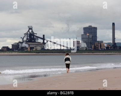 Frau, die am nördlichen Gare-Strand mit einem Redcar-Stahlwerk auf der Südseite der Tess-Mündung im Hintergrund läuft. England. VEREINIGTES KÖNIGREICH Stockfoto