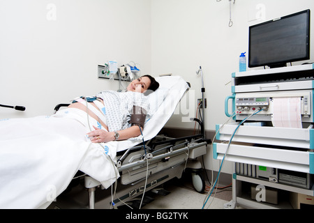 Kaukasische Hispanic Latina schwangeren Verlegung in einem Krankenhausbett Gurney in der Triage-Einheit einen medizinische nicht Stress-Test zu tun. Stockfoto