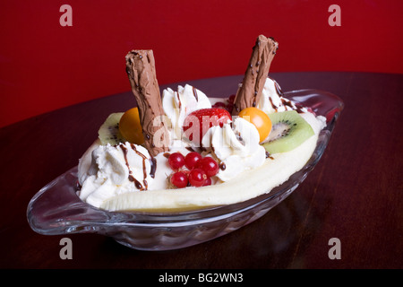 Banana Split mit Kiwis, Erdbeeren, Johannisbeeren, Physalis, Schokolade Flocken, Sahne und Schokoladensauce in einer Petrischale. Stockfoto