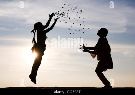 Silhouette von zwei jungen indischen Mädchen springen, werfen und fangen Sternen. Indien Stockfoto