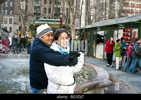 glückliche junge Mischlinge Paar posieren für ein Foto von dem Brunnen im Bryant Park während der Weihnachtszeit in New York City Stockfoto