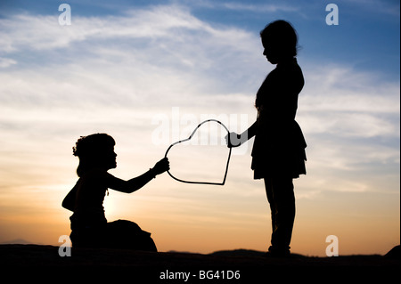 Silhouette von einem zwei junge indische Mädchen geben und nehmen eine Herzform bei Sonnenuntergang. Indien Stockfoto