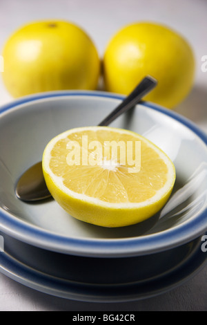 Eine halbe Grapefruit in einer blauen Schüssel und ganze Grapefruits auf einer weißen Tischdecke Stockfoto