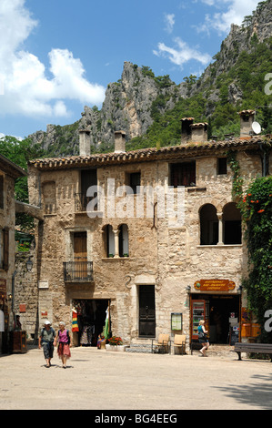 Einige Touristen mittleren Alters laufen über den Dorfplatz mit Souvenirläden, Saint Guilhem le Désert, Hérault, Languedoc Roussillon, Frankreich Stockfoto