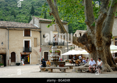 Ein Paar sitzt unter dem Platane Tree auf dem Dorfplatz, Place de la Liberté, Saint-Guilhem-le-Désert, Hérault, Languedoc Roussillon, Frankreich Stockfoto